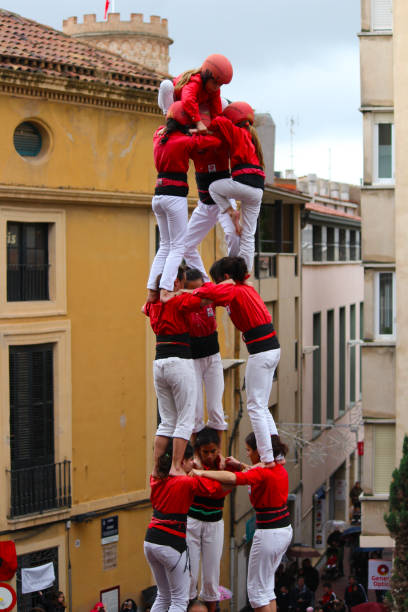 Building Human Towers: The Art and Skill of Castellers “Castells” are human towers, built with a technique that requires great coordination and skill. The people who form part of the castle are called "castellers". The castellers stand on top of each other, forming several floors, until an impressive structure is created that can be very tall. These human towers are built traditionally during the festivals within Catalonia. unesco organised group stock pictures, royalty-free photos & images