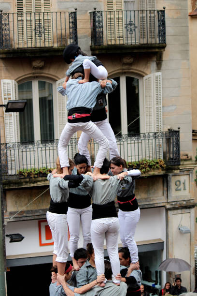 Building Human Towers: The Art and Skill of Castellers “Castells” are human towers, built with a technique that requires great coordination and skill. The people who form part of the castle are called "castellers". The castellers stand on top of each other, forming several floors, until an impressive structure is created that can be very tall. These human towers are built traditionally during the festivals within Catalonia. unesco organised group stock pictures, royalty-free photos & images