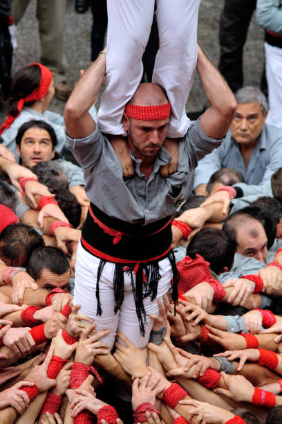 Building Human Towers: The Art and Skill of Castellers “Castells” are human towers, built with a technique that requires great coordination and skill. The people who form part of the castle are called "castellers". The castellers stand on top of each other, forming several floors, until an impressive structure is created that can be very tall. These human towers are built traditionally during the festivals within Catalonia. unesco organised group stock pictures, royalty-free photos & images