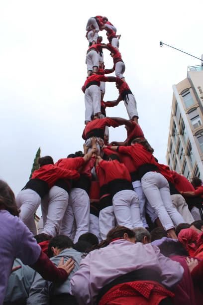 Building Human Towers: The Art and Skill of Castellers “Castells” are human towers, built with a technique that requires great coordination and skill. The people who form part of the castle are called "castellers". The castellers stand on top of each other, forming several floors, until an impressive structure is created that can be very tall. These human towers are built traditionally during the festivals within Catalonia. unesco organised group stock pictures, royalty-free photos & images