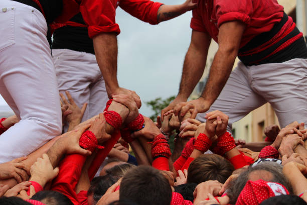 Building Human Towers: The Art and Skill of Castellers “Castells” are human towers, built with a technique that requires great coordination and skill. The people who form part of the castle are called "castellers". The castellers stand on top of each other, forming several floors, until an impressive structure is created that can be very tall. These human towers are built traditionally during the festivals within Catalonia. unesco organised group stock pictures, royalty-free photos & images