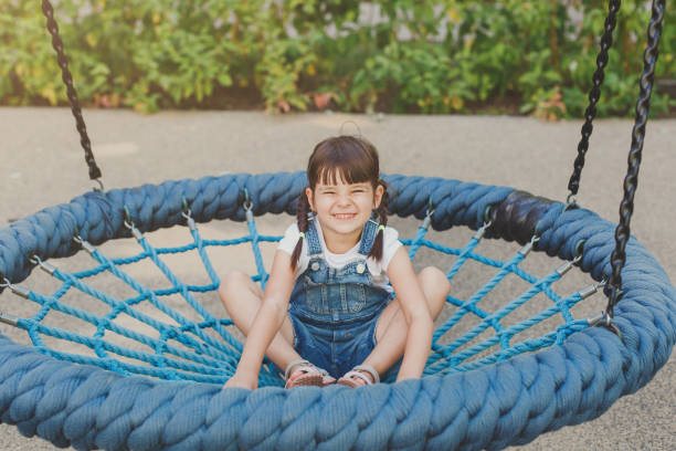 one little cute girl 4 years old sits on a hanging round swing with a net and smiles funny on the playground in summer, childhood concept. - 4 5 years laughing preschooler little girls 뉴스 사진 이미지