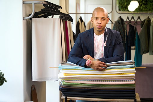 Young tailor leaning on rolls of fabric and looking in front of him