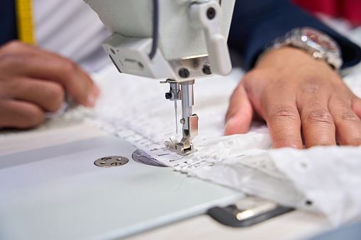 Closeup of dressmaker hands stitching seam on client dress using sewing machine