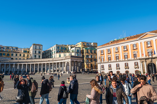 Naples, Italy - December, 18, 2022: A lively public square filled with people, surrounded by ornate historical buildings under a clear blue sky
