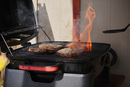 Food, backyard bbq and burger on flame, flipping patties on fire for fun social gathering and weekend time. Meat, cooking burgers and outdoor hamburger grilling for barbecue party or cookout at home.