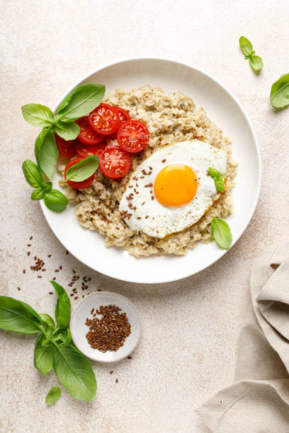 istock Oatmeal with fried sunny-side-up egg, tomatoes and basil, top view 2043604341