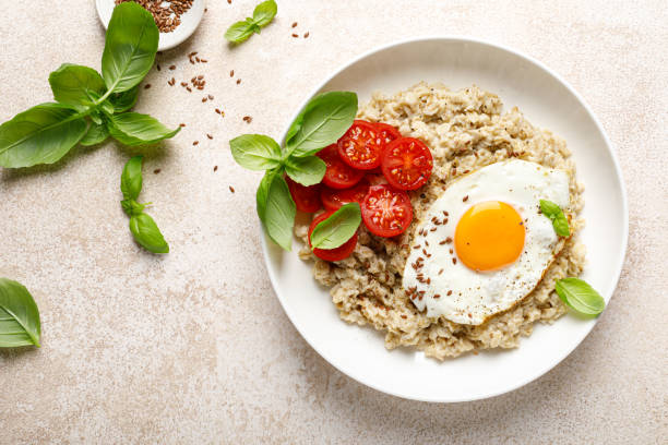istock Oatmeal with fried sunny-side-up egg, tomatoes and basil, top view 2043604347