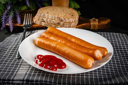 Frankfurter sausages with ketchup on a white plate.