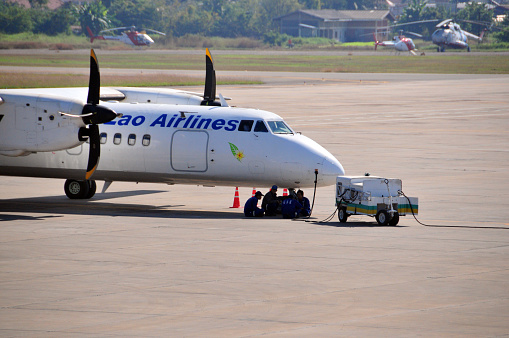 Sikhodtabong District, Vientiane Prefecture, Laos:  Lao Airlines, the state airline of Laos, made in China Xi'an MA-60 (registration RDPL-34171, MSN 0507), Wattay International Airport. The MA-60 is turboprop-powered airliner produced by China's Xi'an Aircraft Industrial Corporation under the Aviation Industry Corporation of China (AVIC), it is a derivative of the Soviet Antonov An-24, via the Xi'an Y7-200A.  The aircraft, designed for regional and feeder services, is designed as a shoulder-wing aircraft and is powered by two Pratt & Whitney Canada PW127J turboprop engines. Front part of the aircraft with ground equipment and ground crew escaping the scorching heat under the fuselage.