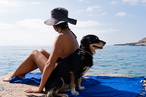 Beautiful image of an unrecognizable woman with a hat and in a bikini sunbathing on a pier with her pet dog on a beautiful summer day on the Greek island of Crete