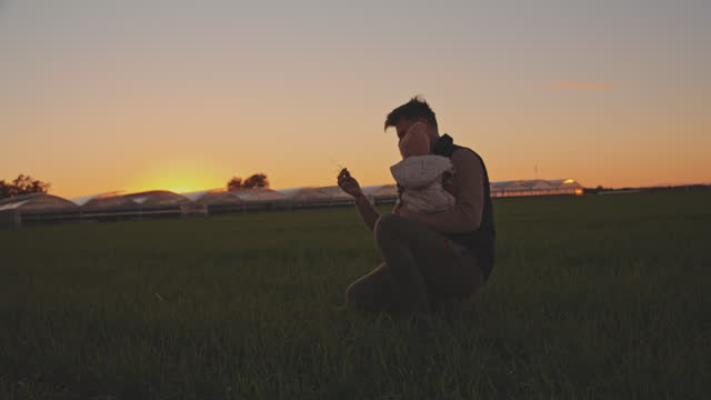 SLO MO Male Farmer Showing Grass to Baby while Crouching on Agricultural Field during Sunset