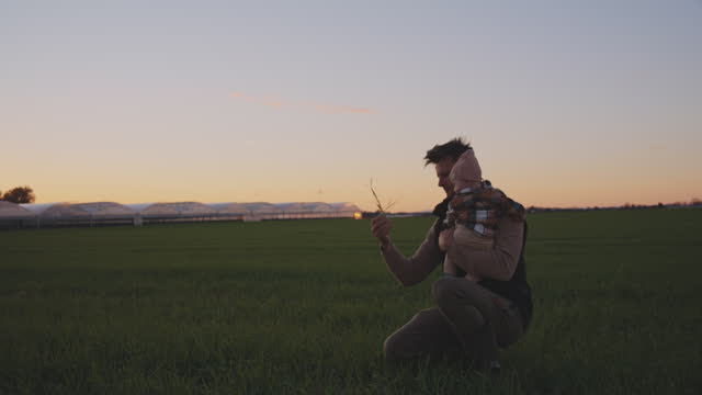 SLO MO Male Farmer Carrying Baby and Showing Grass to him on Agricultural Field against Clear Sky during Sunset