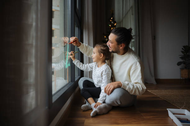 Father with daughter decorate a window in the living room in anticipation of the new year.