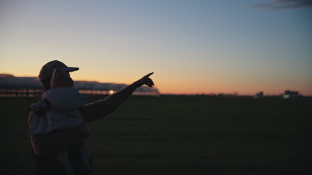 SLO MO Farmer Showing Agricultural Field and Greenhouse to Baby while Carrying him against Blue Sky during Sunset