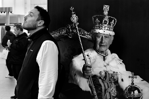 London, United Kingdom - February 22 2024: Man standing in front of a poster of King Charles III in Kings Cross train station in London, in black and white