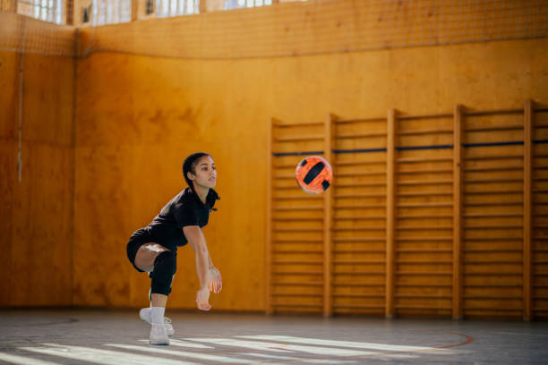 A multicultural teenage female volleyball player is practicing and digging the ball on volleyball training on court. A professional volleyball player is digging the ball on volleyball training.