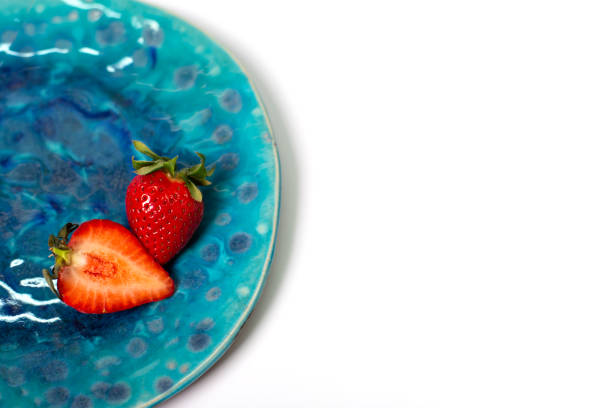 Blue ceramic plate with a pair of red strawberries on a white background.