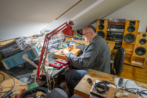 Senior man using a soldering iron medtronic at home while listening music in background