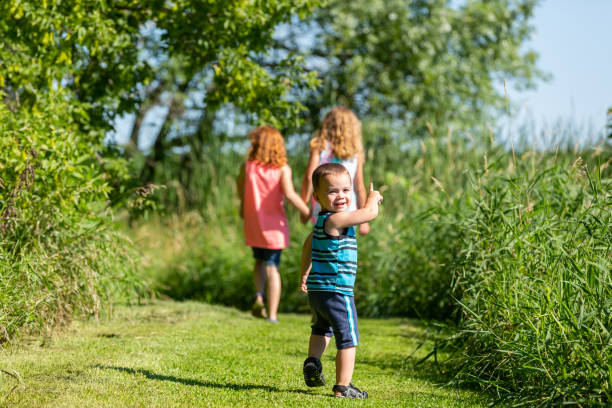 Little boy following his sisters as they go for a walk on a rural farm.