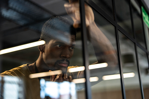 Mid-shot profile view of young African American businessman thinking and looking through the window inside office
