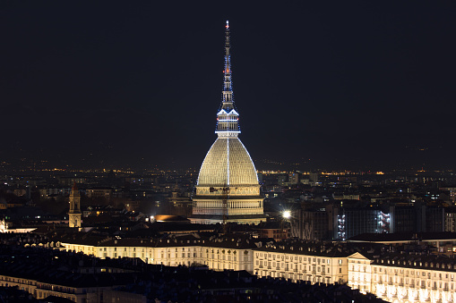 Turin's cityscape at night, particularly its iconic monument, the Mole Antonelliana, illuminated by special Christmas lights.