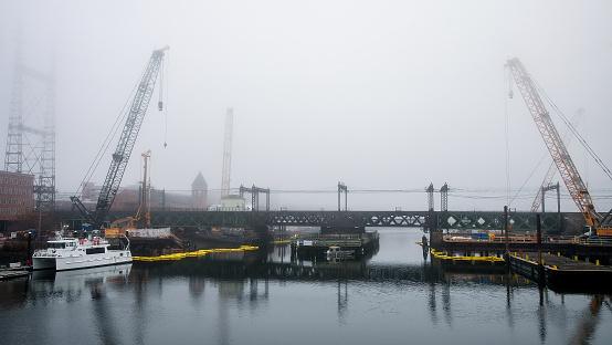 Norwalk, CT, USA - February 27, 2024: View from bridge over Norwalk river in fogy winter day with construction site and boat