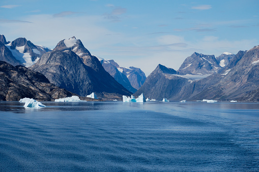 Jagged and glaciated mountains of East Greenland are surrounded by icebergs and a brilliant blue sea