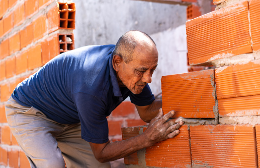 Senior man building a brick wall at a construction site - Construction industry concepts