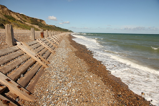 Coastal sea defences wooden breakwaters on shingle beach on bright sunny day