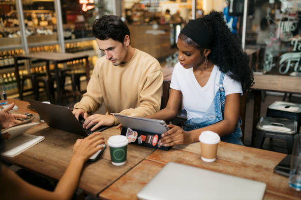 istock Two diverse friends sitting at cafe table with laptop and digital tablet 2043985243