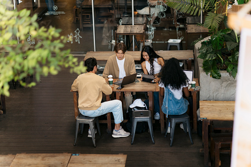 Group of multiethnic friends working together in cafe. Multiracial group of young people sitting at cafe table using laptop and digital tablet.