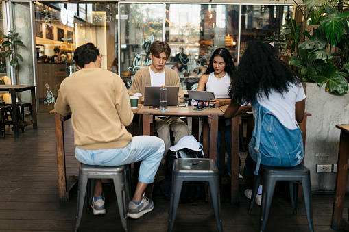 Group of diverse friends working in cafe. Multiracial college students sitting at cafe table using laptop and digital tablet.