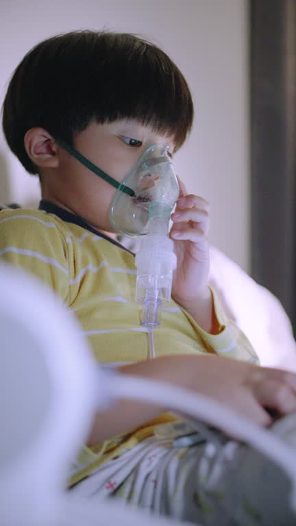 Little boy is having a medicine inhalation while watching a tablet in the bedroom at home