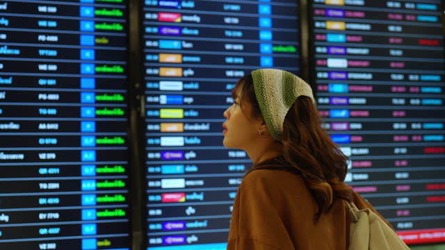 4K Asian woman looking timetable at airport terminal.