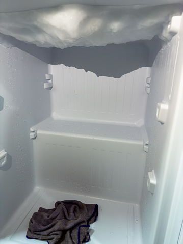 the mesmerizing formation of ice inside a freezer, presenting a natural sculpture reminiscent of a frozen cave. A cloth lies forgotten on the freezer's floor, contrasting with the icy canopy above. The image invites contemplation of the cold beauty and the fascinating shapes tha