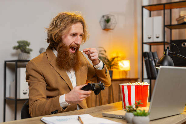 istock Businessman eating popcorn while playing video game on laptop spending leisure time at home office 2044073047