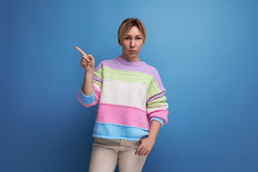 serious blond young woman in a striped sweater shows her hand in on a blue background.