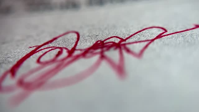 Very close up of the tip of a red pen signing on a white paper