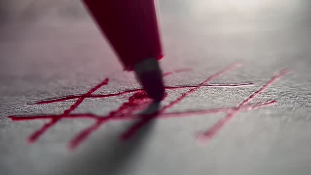 Very close up of the tip of a red pen writing on a white paper
