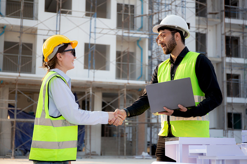 Team architect or engineer holding laptop looking model house and doing agreement while handshake together at construction site, contractor and partner discussion and planning about of real estate.