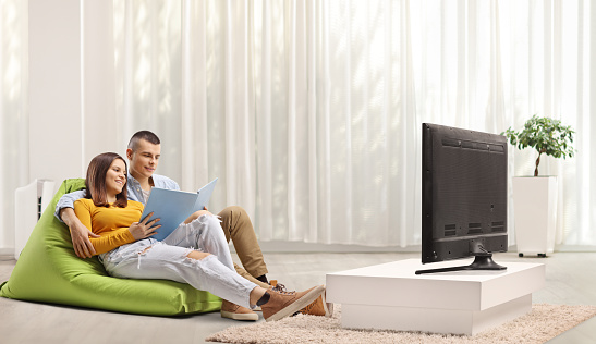 Young couple sitting on a beanbag and reading a book in front of tv