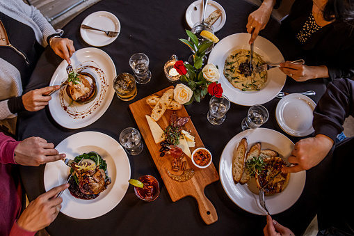 A small group of four adults sit together in a restaurant as they enjoy a meal together.  They each have a dish out in front of them in this aerial view of their table.