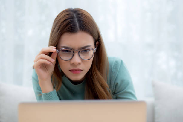 istock Concentrated young asian woman wearing glasses working on laptop with commitment and ambition sitting on sofa in living room at home, work from home, freelance working online, business and lifestyle. 2044197418