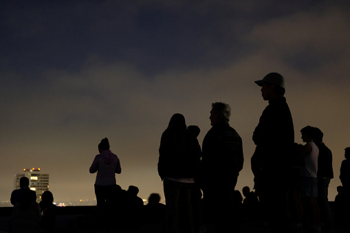 Mixed group of people hanging out on rooftop deck at a party or get together to enjoy an evening under the clouds.