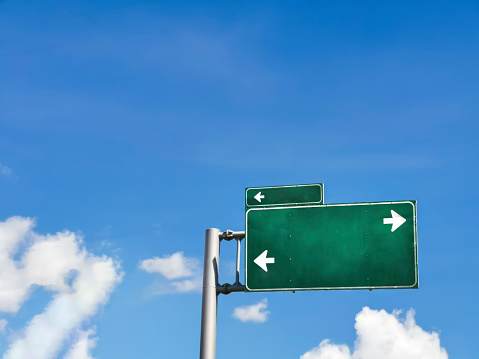 Blue sky with clouds and a green traffic sign with white direction arrows, signage and journey theme, horizontal image