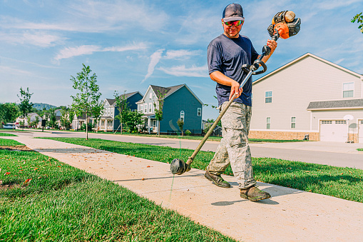 Man using a Weed Trimmer to Edge a Sidewalk in a Modern Apartment Neighborhood