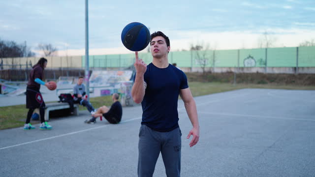 SLO MO Portrait of Confident Young Man Spinning Streetball on Finger and Looking At Camera on Basketball Court