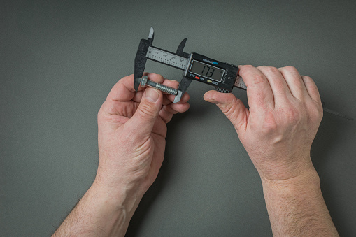 Men's hands measure the screw using an electronic caliper. A tool for accurate measurement of dimensions.
