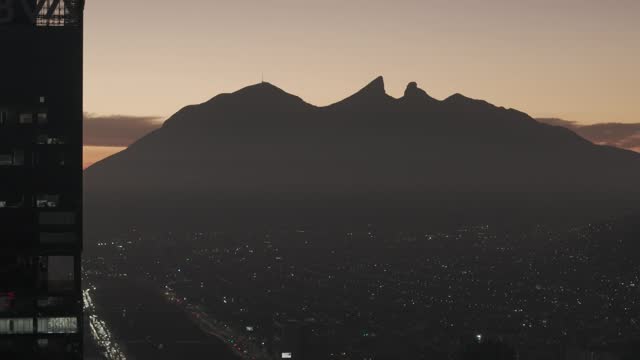 Aerial revealing shot of the Cerro de la Silla from behind a skyscraper at dusk